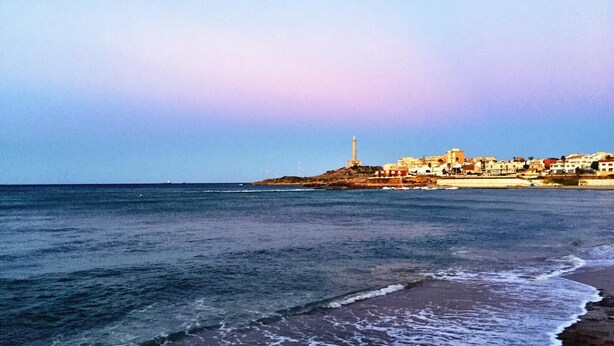 A coastal town with a lighthouse, sandy beach, and buildings along the shore.