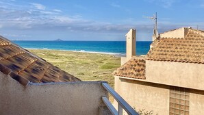 A coastal view with a clear sky, a distant mountain, and a building with a tiled roof and satellite dish. - Large terrace 140m from the Mediterranean Sea (Cabo de Palos)