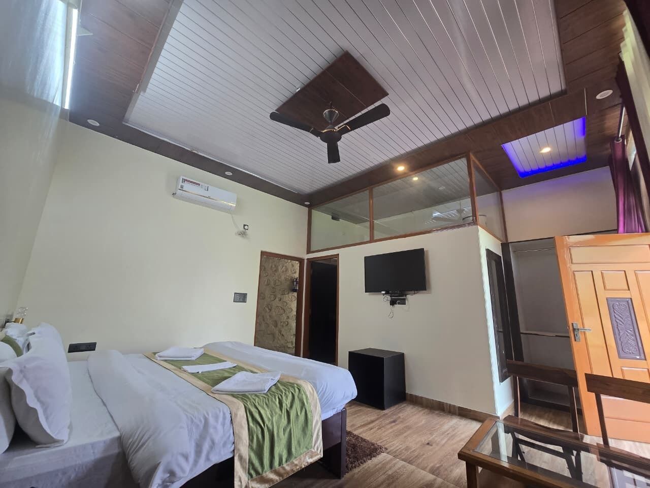 A hotel room with a bed, a ceiling fan, a TV, and a wardrobe.