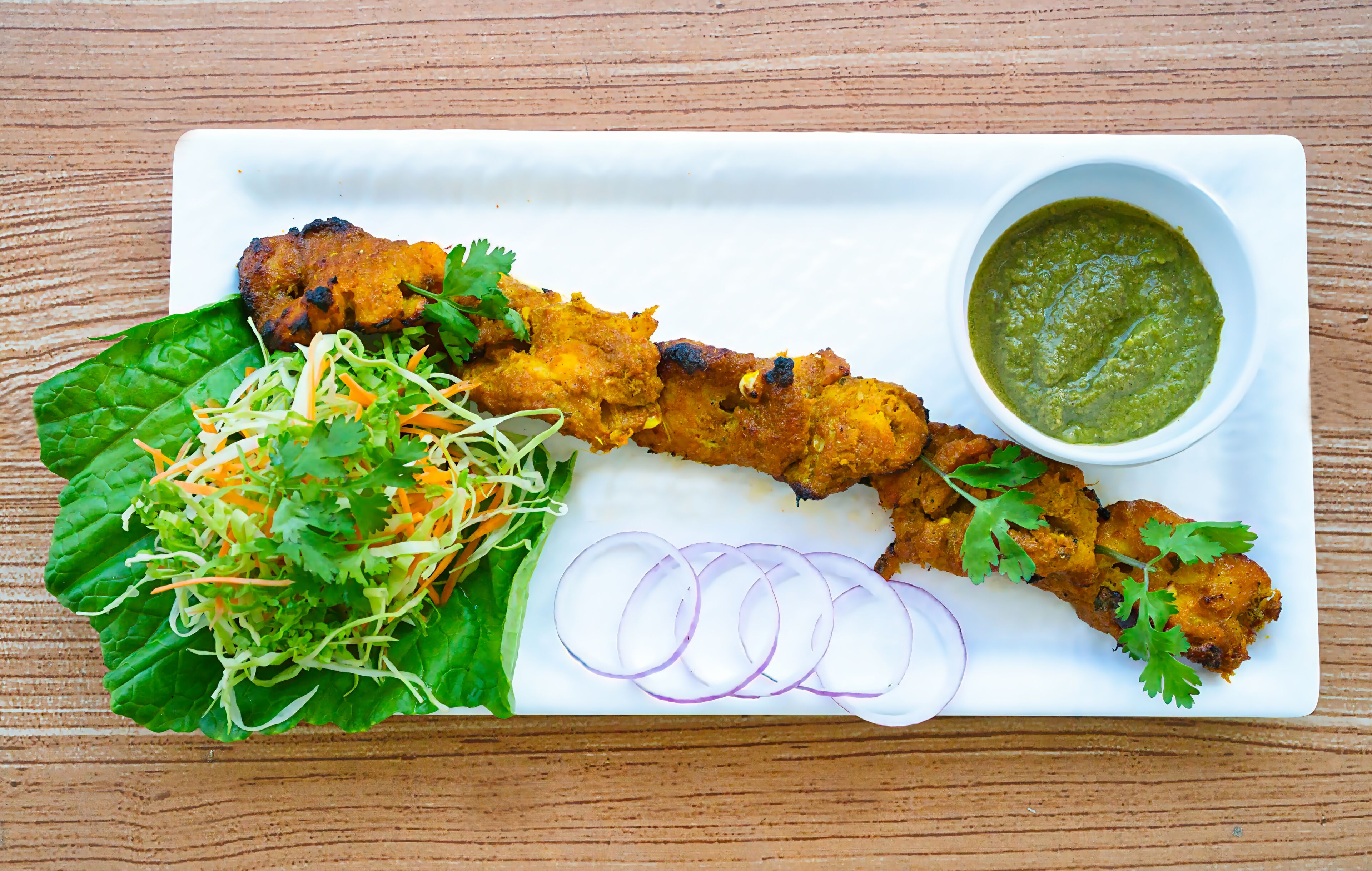 A plate with grilled chicken, a side salad, sliced onions, and a green sauce.