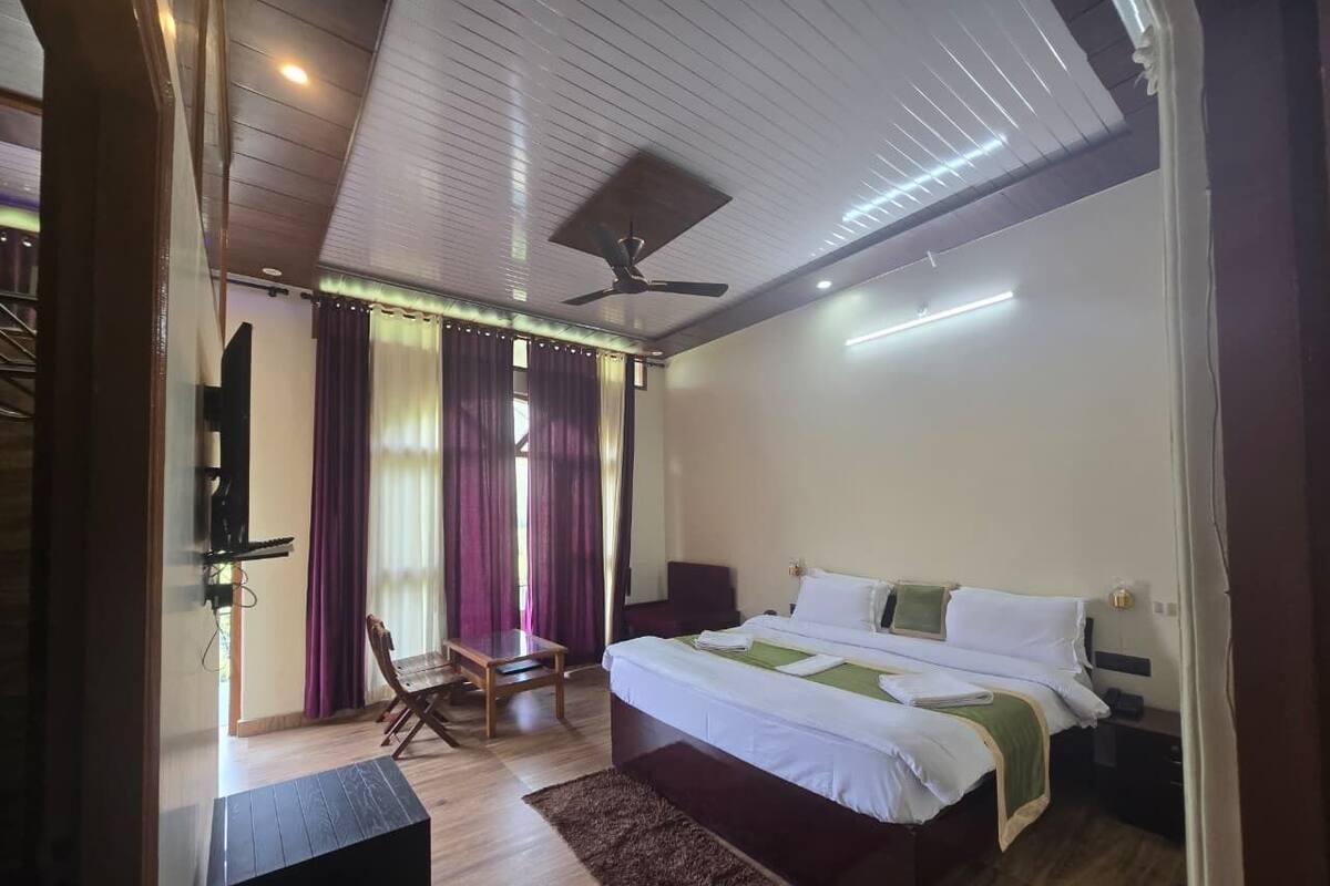 A bedroom with a bed, a desk, a chair, a ceiling fan, and a window with curtains.