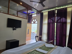 A bedroom with a bed, a television, a ceiling fan, and a window with curtains.