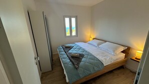 A bedroom with a bed, a window, a bedside lamp, and a door.