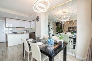 Una cocina moderna con armarios blancos, una zona de comedor con mesa de vidrio y un espejo que refleja la cocina.