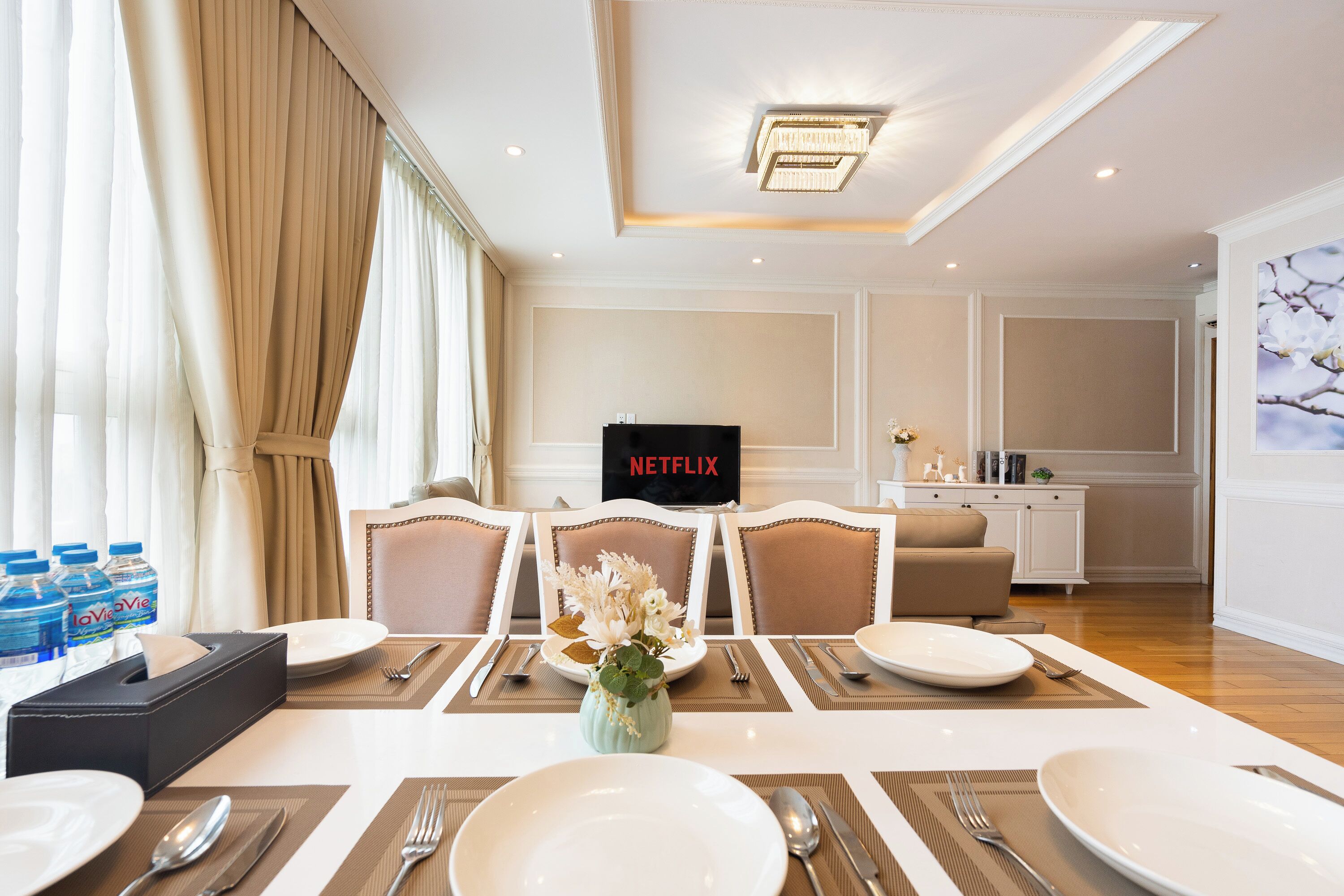 Een restaurantgedeelte in een hotel, met een tafel voor vier personen, een bloevas en een Netflix-bord aan de muur.