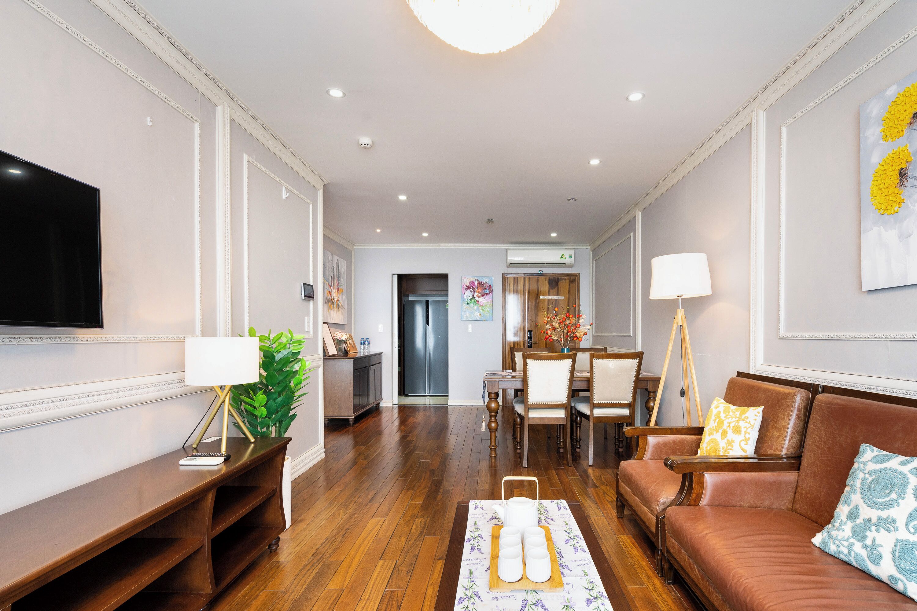 A hotel lobby with a wooden reception desk, a television, a seating area with a sofa and chairs, and a dining area with a table and chairs.