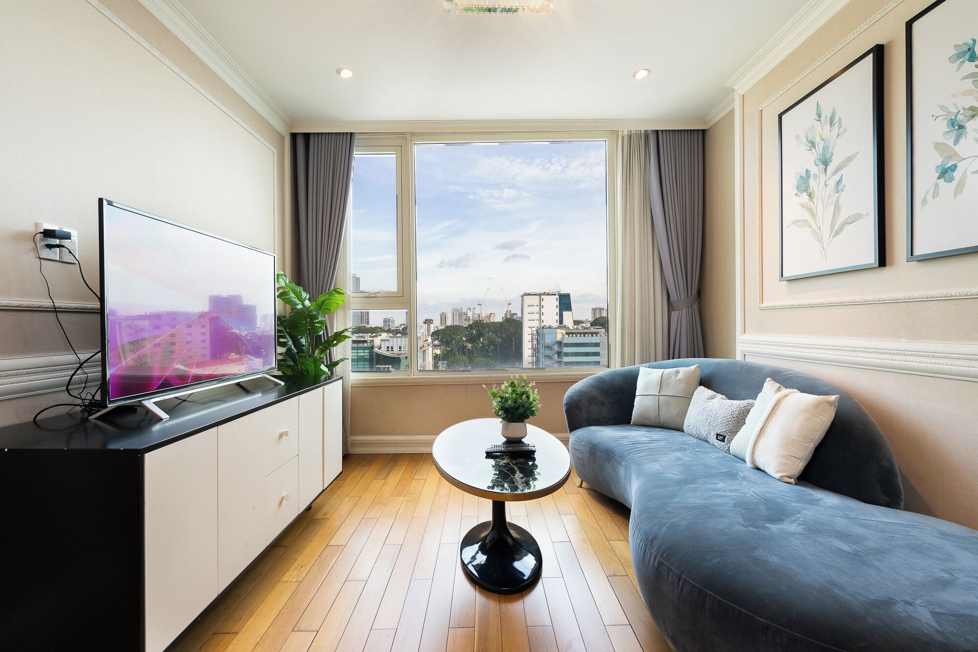 A modern living room with a flat-screen TV, a sofa, a coffee table, and a large window with a city view.