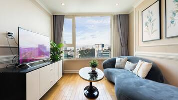 A modern living room with a flat-screen TV, a sofa, a coffee table, and a large window with a city view.