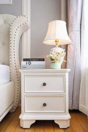 Une table de chevet blanche avec une lampe, une pile de livres et un vase rempli de fleurs.