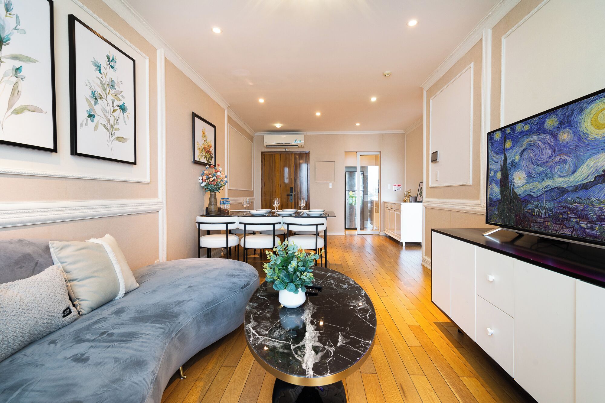 A modern living room with a sofa, a dining table with chairs, a TV, and artwork on the walls.