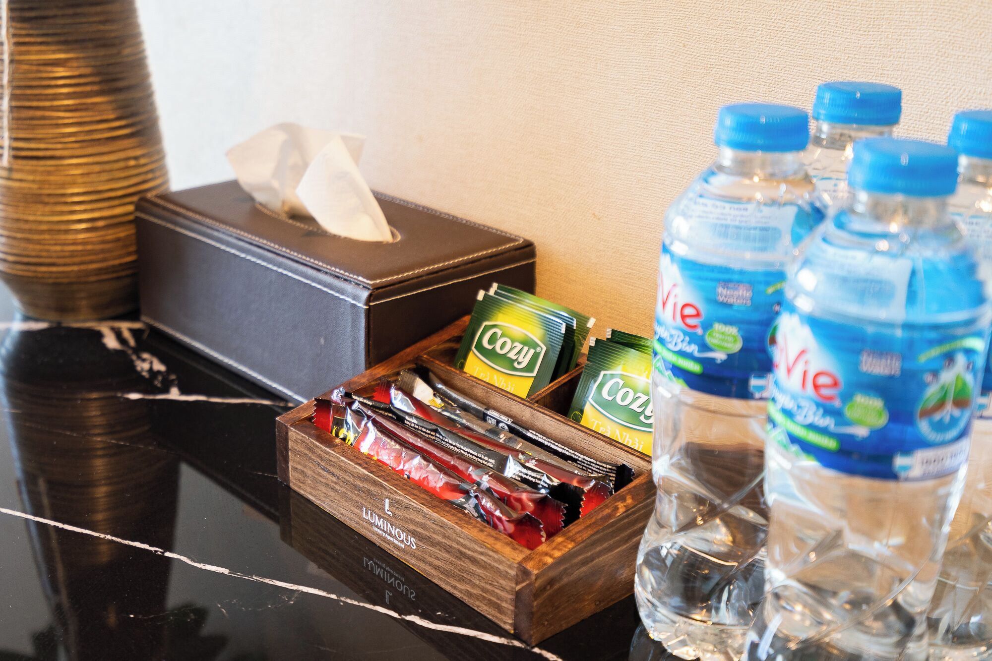 A hotel room with a wooden box containing snacks, a tissue box, and bottled water.