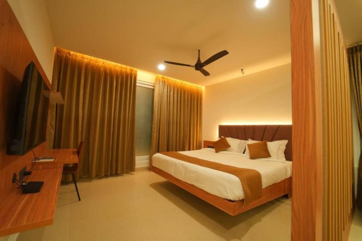 Una habitación de hotel con cama, escritorio, silla, televisor y ventilador de techo.