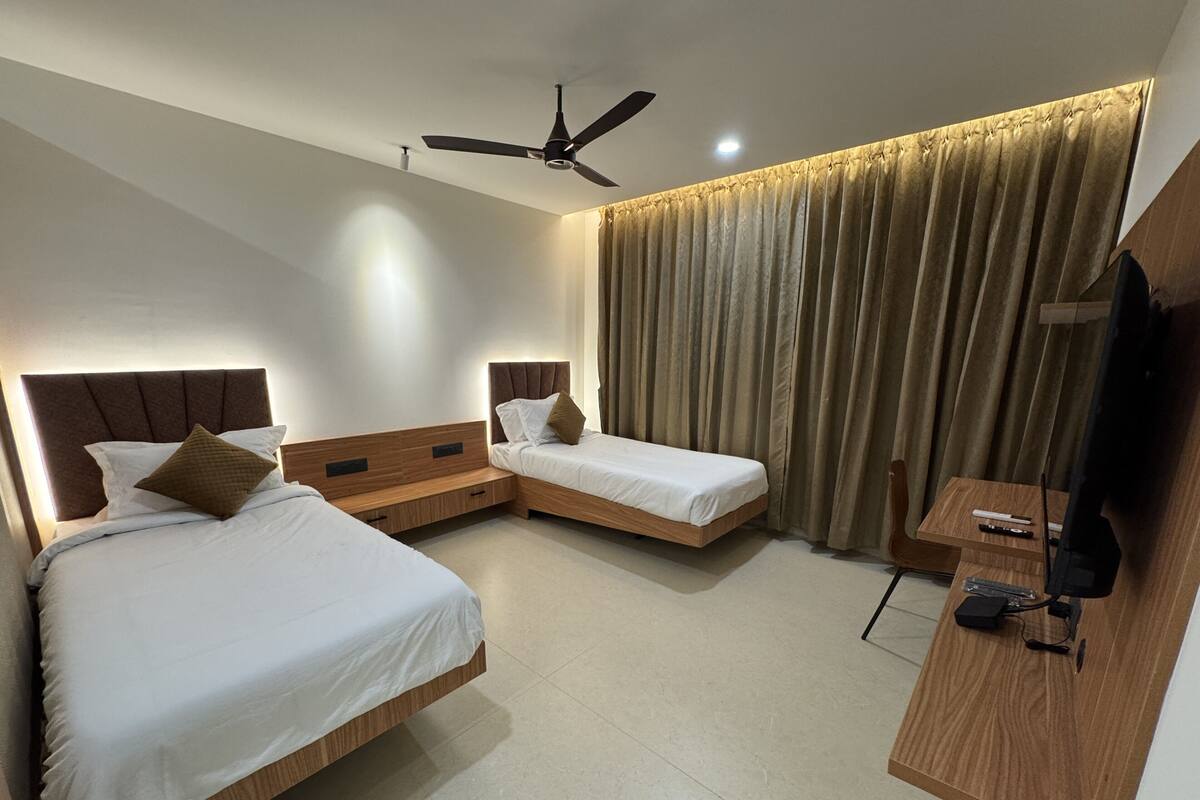Habitación de hotel con dos camas individuales, un ventilador de techo, un televisor y un escritorio.