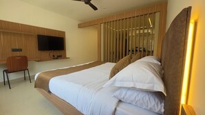 A hotel room with a bed, a TV mounted on the wall, a desk, and a chair. - Arunaragha (Mysore)