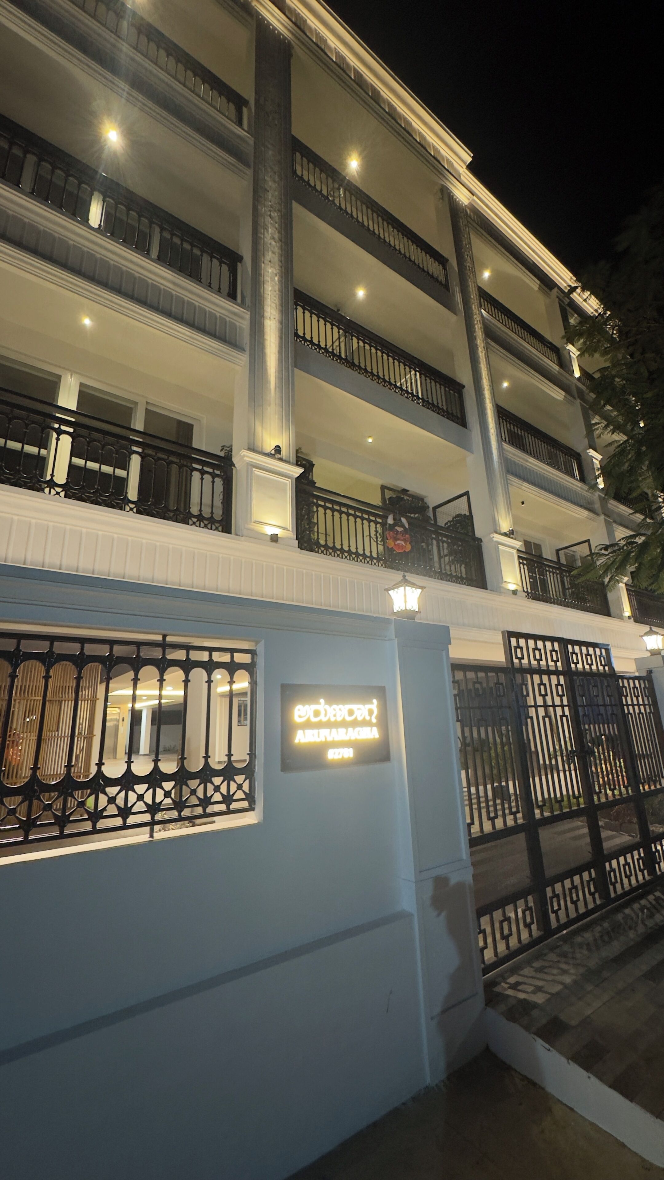 A multi-story building with a balcony on the second floor, a sign with illuminated text, and a gated entrance.