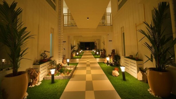 A hotel corridor with a checkered floor, potted plants, and wall-mounted lights. - Arunaragha (Mysore)