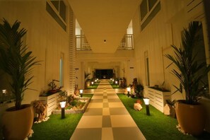 A hotel corridor with a checkered floor, potted plants, and wall-mounted lights. - Arunaragha (Mysore)