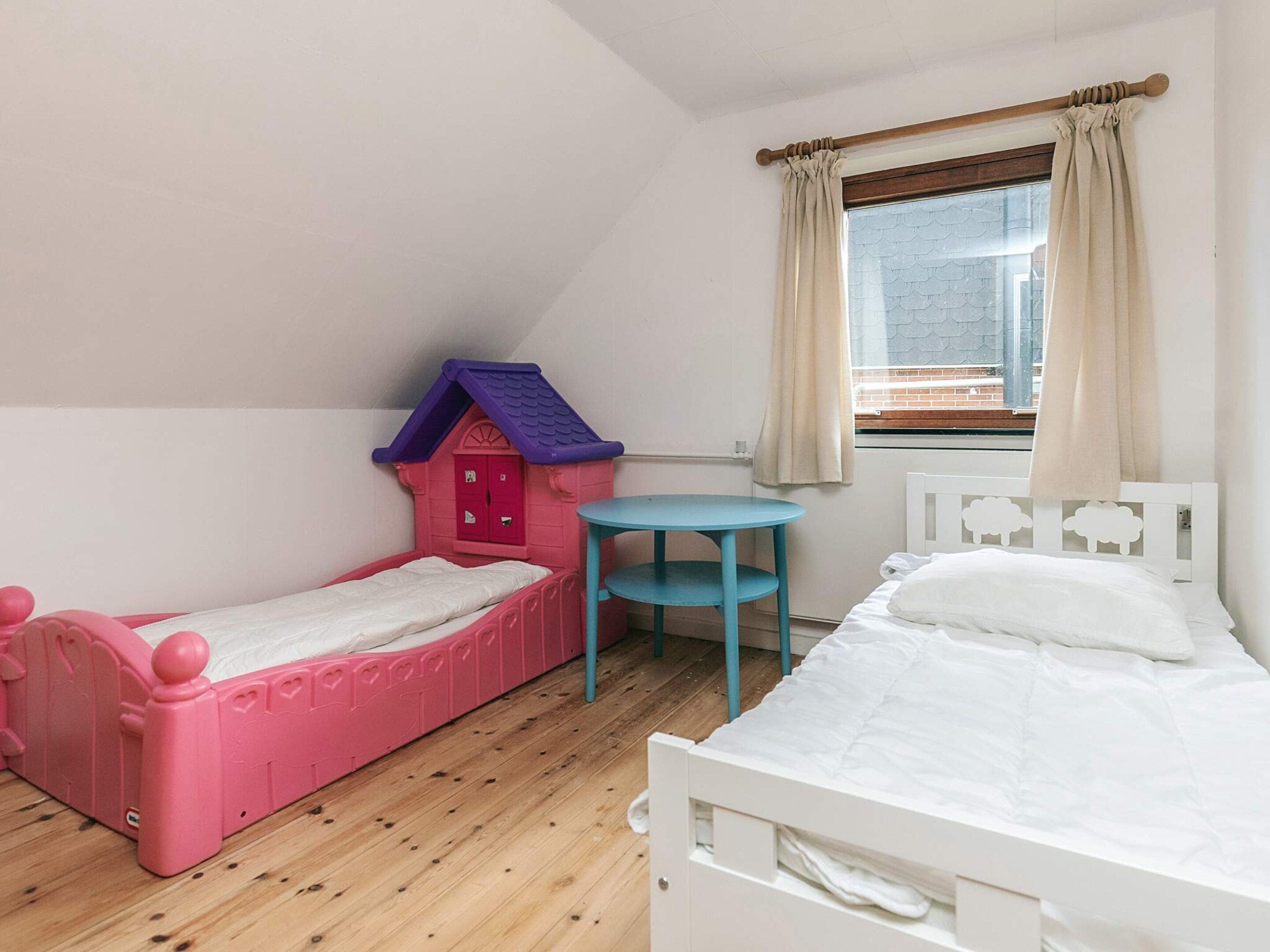 A child's bedroom with two beds, a small table, and a playhouse.