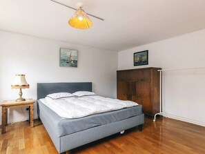 Une chambre à coucher avec un lit, une table de chevet en bois avec une lampe, une armoire et deux tableaux accrochés au mur.