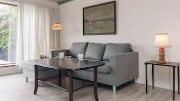 A living room with a grey sofa, a wooden coffee table, a lamp on a side table, and a painting on the wall.