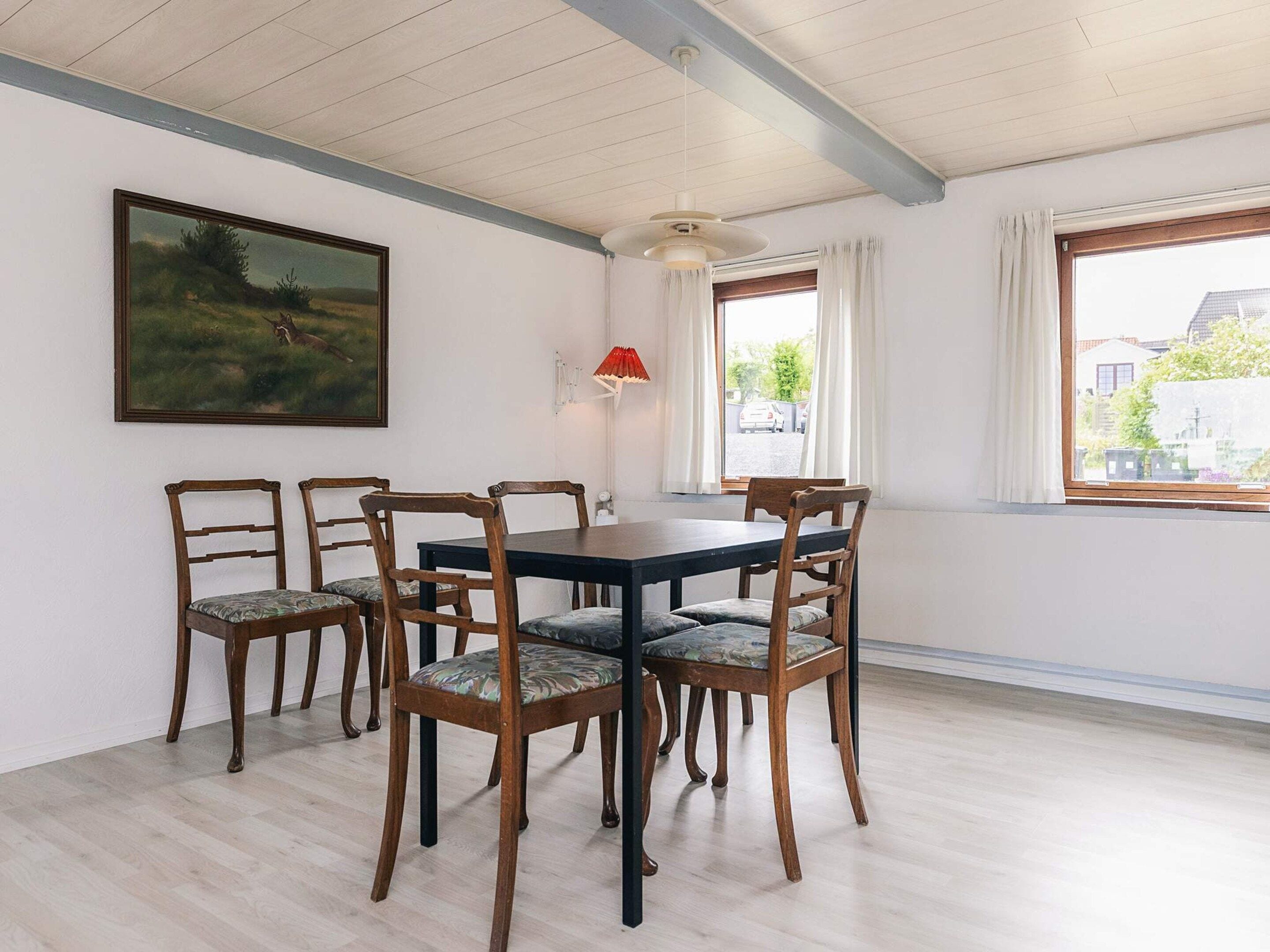 A dining area with a table and chairs, a painting on the wall, a window with curtains, and a lamp.