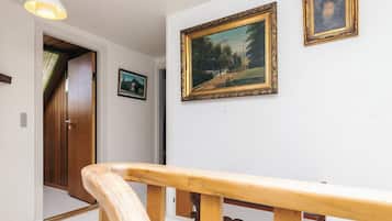 Un pasillo con puerta de madera, pared blanca y dos cuadros enmarcados, y barandilla de madera.