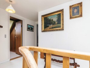 A hallway with a wooden door, a white wall with two framed pictures, and a wooden railing.