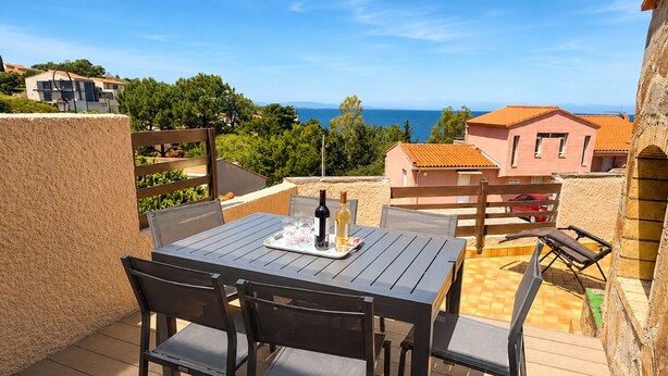 Een terras met een tafel gedekt voor twee personen, een fles wijn en glazen.