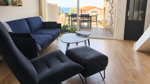 Een woonkamer met een bank, twee fauteuils, een kleine tafel en uitzicht op de zee door een glazen deur.