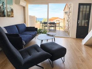 A living room with a sofa, two armchairs, a small table, and a view of the sea through a glass door. - Comfortable apartment with AC - 4 guests (Collioure)