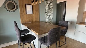 Een moderne keuken met een houten keukeneiland, twee barkrukken, hanglampen, een koelkast, en een citaat in een lijst op de muur.