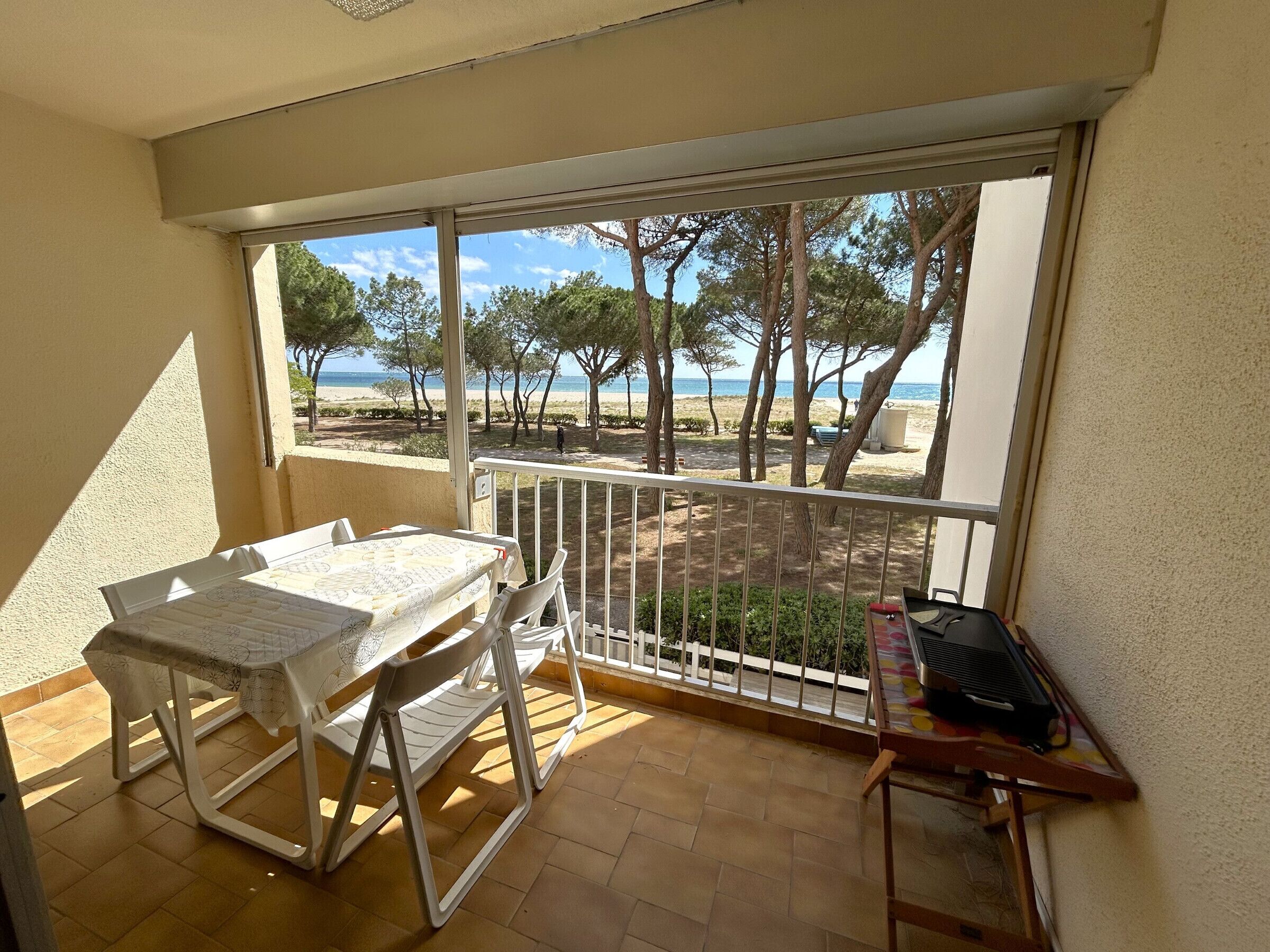 Un balcon avec une table et des chaises, un barbecue et une vue sur la plage et les arbres.