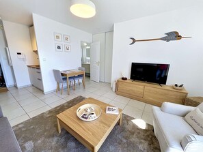 Un salon moderne avec une table basse en bois, un canapé, un téléviseur posé sur un meuble en bois, et un coin repas comprenant une table et des chaises.