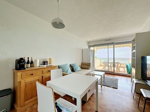 Ein modernes Wohnzimmer mit Essbereich, Küchenzeile und einer großen Glasschiebetür, die auf einen Balkon mit Meerblick führt.