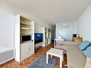 Ein Wohnzimmer mit Fernseher, Sofa, Couchtisch und einer Essecke mit Tisch und Stühlen.