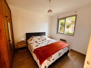 Ein Schlafzimmer mit Bett, Nachttisch, Fenster und Heizkörper.