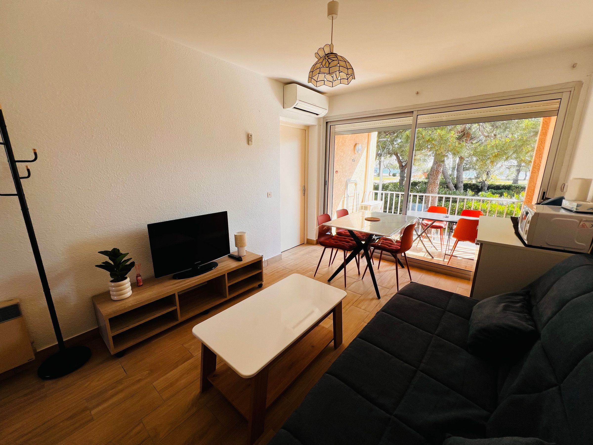 Una sala moderna con una televisión de pantalla plana, una mesa de centro de madera, un sofá y un comedor con una mesa y sillas.