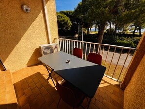 A balcony with a table and chairs, a security camera, and a view of trees and a road. - Apartment, AC, sea view - 4 guests (Argelès-sur-Mer)
