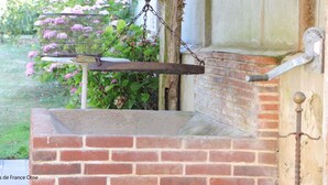 A brick oven with a hanging scale, a metal door, and a brick wall. - Charming house in the heart of Perche - 4 guests (Longny-au-Perche)