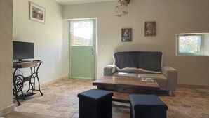A living room with a television, a sofa, a coffee table, and a door. - Charming house in the heart of Perche - 4 guests (Longny-au-Perche)