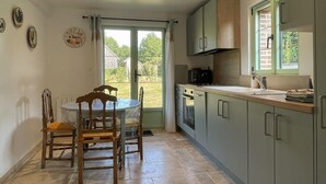 A kitchen with a dining table, chairs, cabinets, a window, and a view of the outdoors. - Charming house in the heart of Perche - 4 guests (Longny-au-Perche)