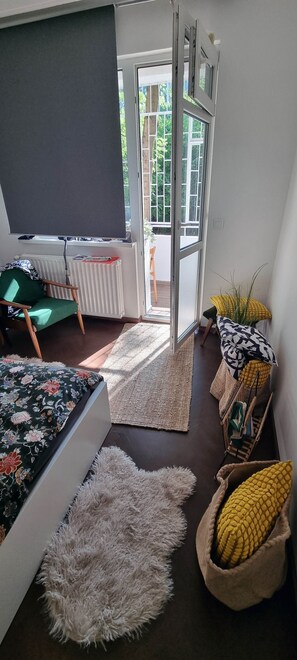 Une pièce comprenant un lit, une chaise, une petite table, un radiateur, une fenêtre et une porte donnant sur l’extérieur.