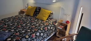 A bed with floral bedding, two yellow pillows, a bedside table with a book, and a wicker basket. - 2-bedroom apartment in wonderful vintage Sofia with AC and comfort (Sofia)