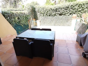 Eine Terrasse mit Tisch und Stühlen, umgeben von einem Heckenzaun und einem weißen Gitter.