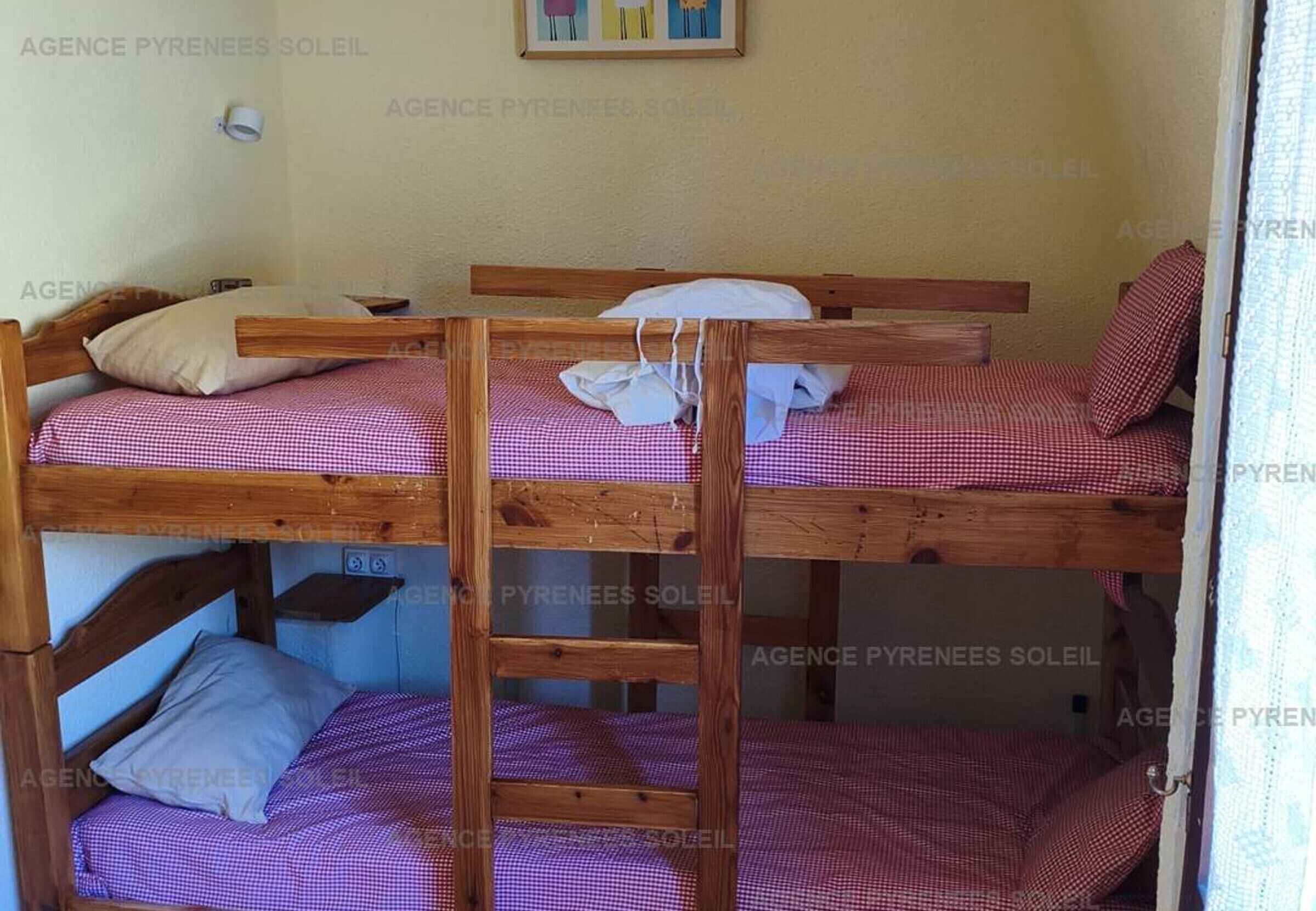 Habitación con literas de madera, ropa de cama a cuadros y una pequeña estantería.