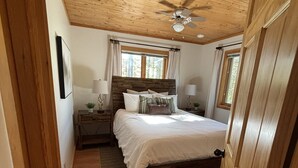 A wooden-paneled bedroom with a bed, nightstands, and a ceiling fan.
