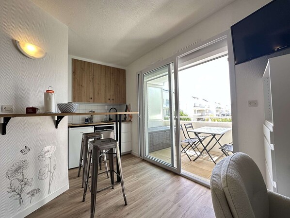 A modern kitchen with wooden cabinets, a dining area with a table and chairs, and a sliding glass door leading to a balcony. - Studio in Minimes, parking - 2 guests (La Rochelle)