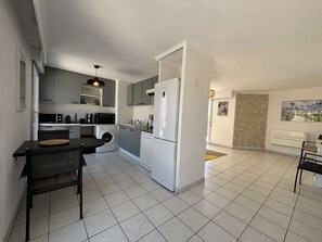 A modern kitchen with a washing machine, a dining area with a table and chairs, and a stone accent wall. - Apartment with sea view - 4 guests (Cavalaire-sur-Mer)
