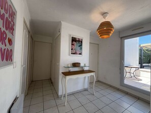 A hallway with a white door, a glass shelf with a basket, a framed picture, and a hanging light fixture. - Apartment with sea view - 4 guests (Cavalaire-sur-Mer)