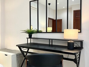 Ein modernes Zimmer mit Schreibtisch, Stuhl, Lampe, Topfpflanze und einem großen Spiegel.
